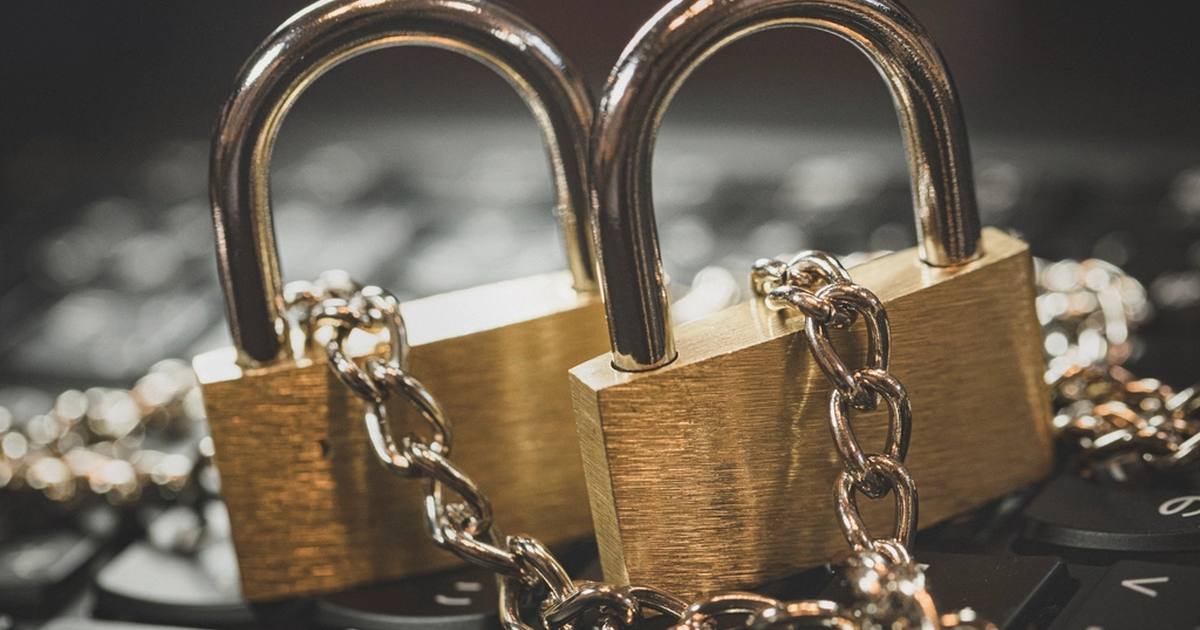 Two brass padlocks wrapped in metal chain resting on a dark laptop keyboard